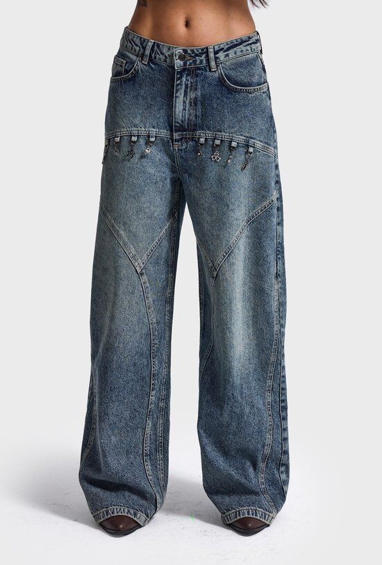 Blauwe, wijde, middelhoge jeans met patchwork-details en zilverkleurige bedeltjes die aan de tailleband hangen.
