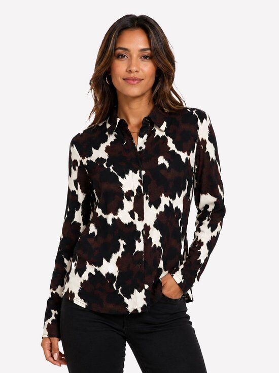 Model draagt damesblouse met lange mouwen in koeienprint in bruin, zwart en wit.