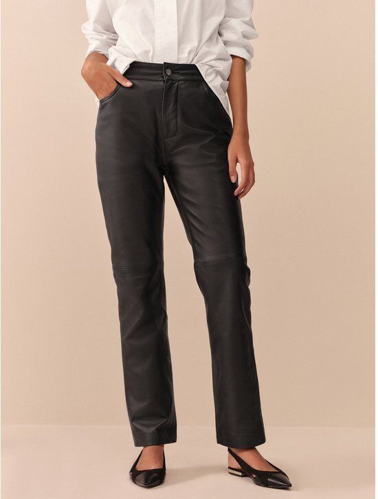 Close-up van een model die een zwarte leren broek met witte blouse en zwarte schoenen draagt.